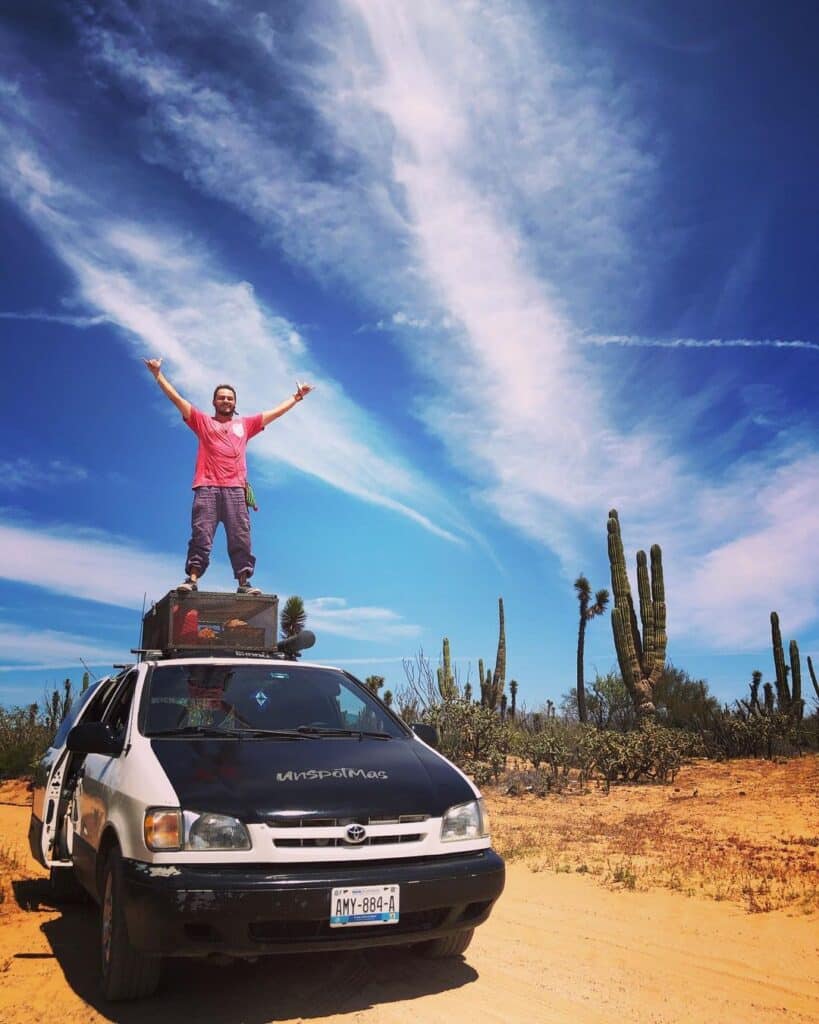 @1unspotmas Man standing on the roof of his campervan parked in the desert
