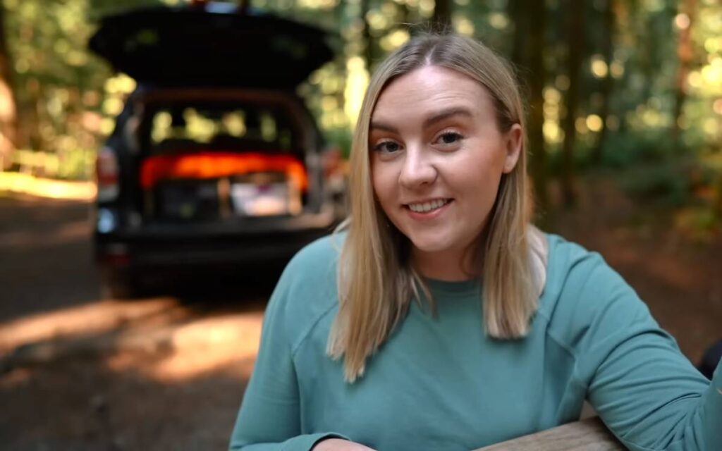 @allisonanderson smiling at the camera with her subaru forester camper conversion in the background