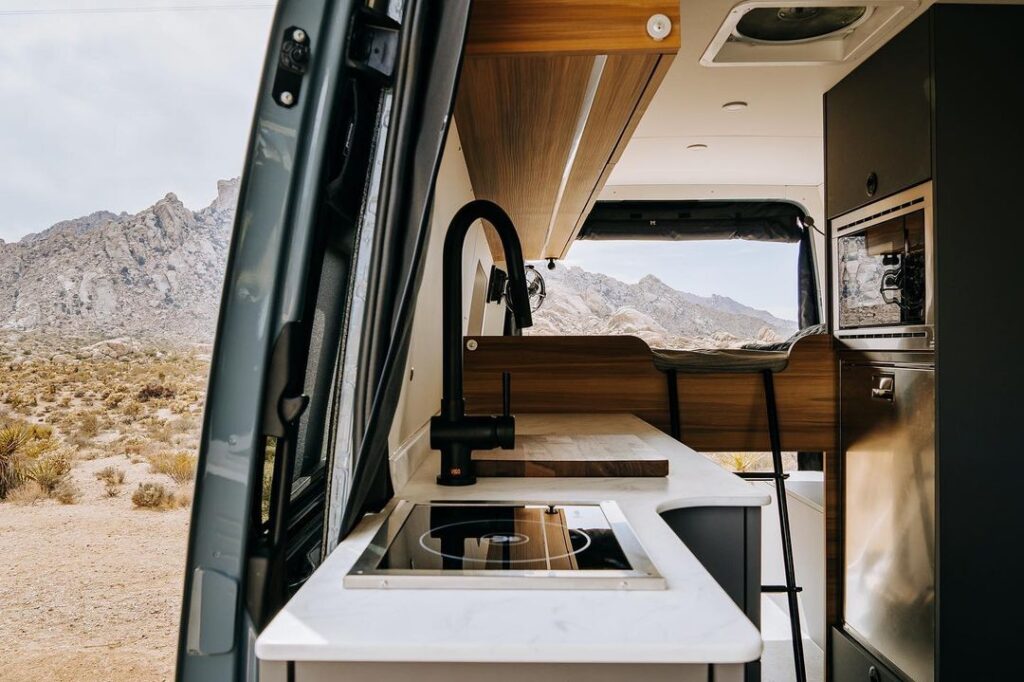 @altcamp interior of campervan highlighting sink and stove with a scenic view of mountains in the background