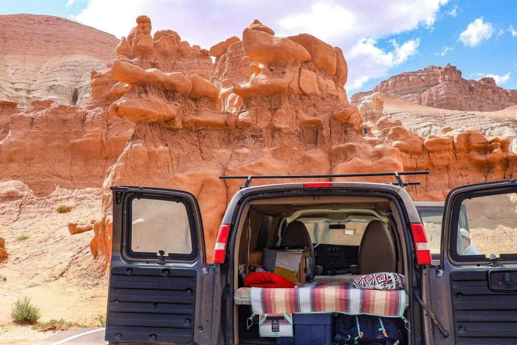 @basecampervans camper van rentals back view with open door, parked near rock mountains