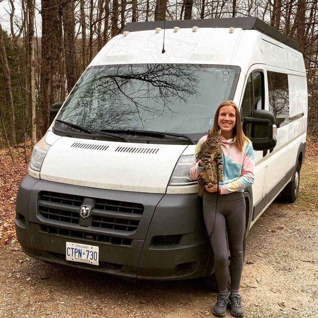 @caren_loves_vans Woman holding a cat while standing against a white van parked in the forest