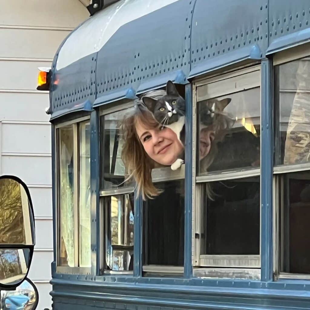 @the_skooligans Woman and her cat sticking their heads out of the window of a blue skoolie 