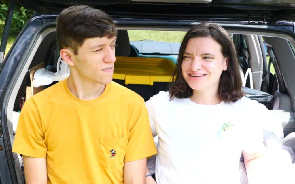 @thearter12 Nicole and Matt smiling and looking at each other while sitting at the back of their SUV camper, forester conversion