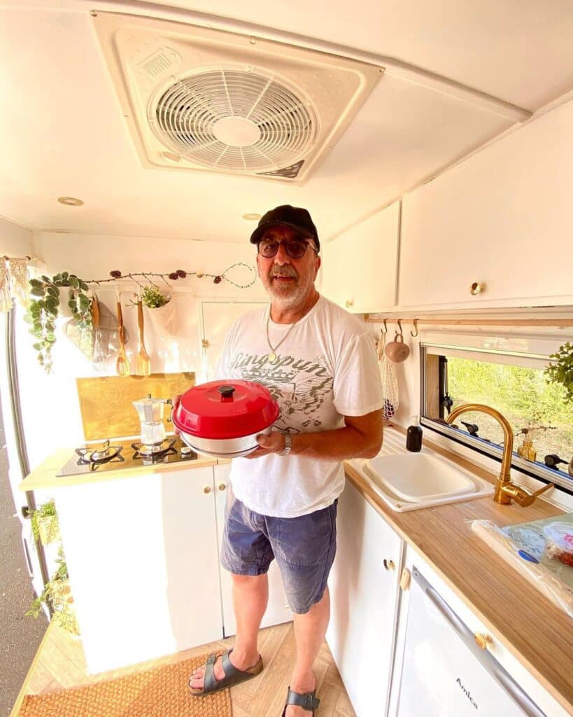 @thegoodlifevan Man holding a portable oven inside his campervan kitchen