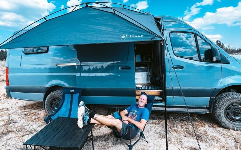 @wanderfulrevolution Nomad sitting on a camping chair with his feet up next to a blue van