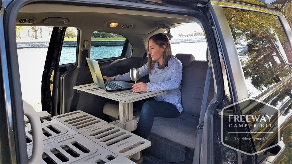 Freeway Camper Kit conversion kit installed in a vehicle, woman using her laptop inside 