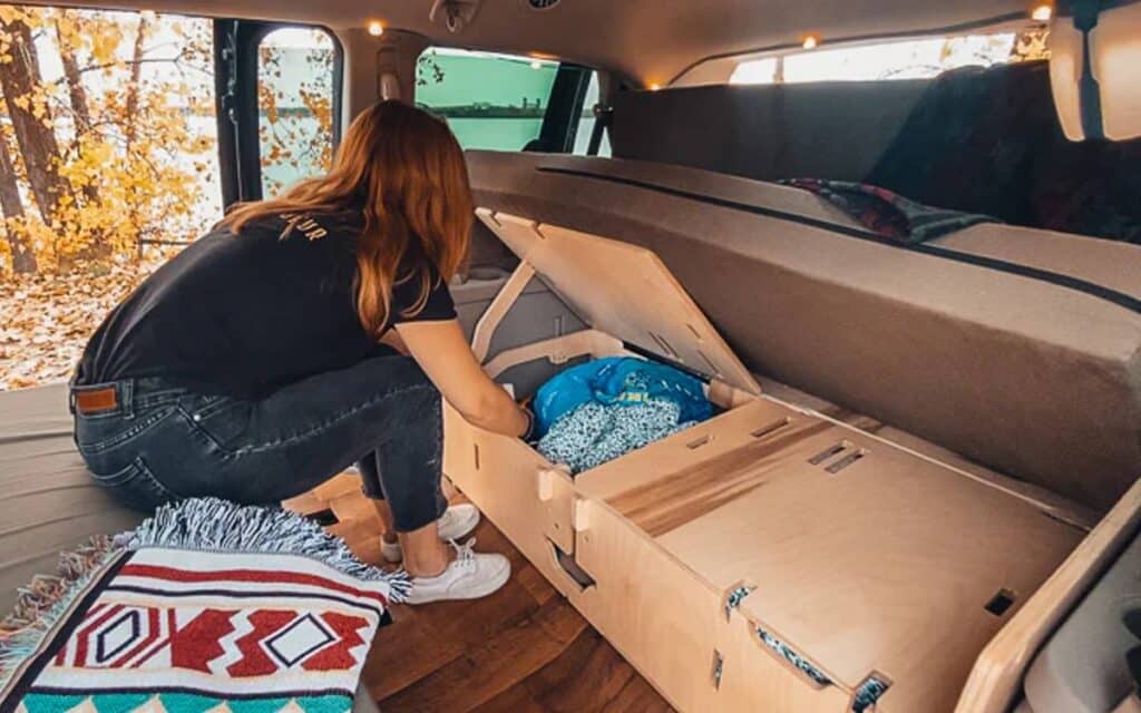 Woman in a camper organizing her under bed storage, a conversion kit from Vanpackers 