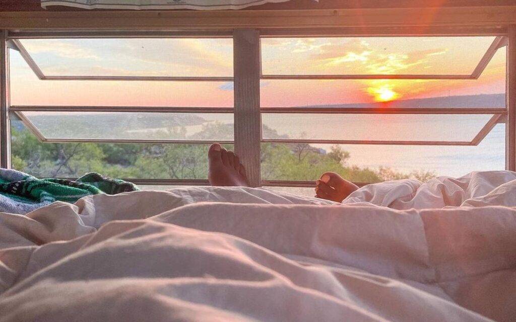 @doesthiscountasvanlife POV of a woman lying on bed alone inside her van, watching the sunrise through the window