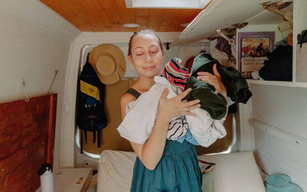 @travelingjam Smiling young woman holding a pile of clothes inside her van