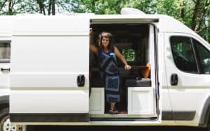 Woman standing in the door of a big white van that could be a sprinter, transit, or promaster