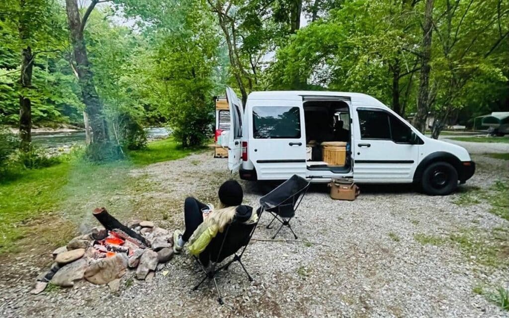 @naomipiercey Woman camping near a river with her white ford transit connect van