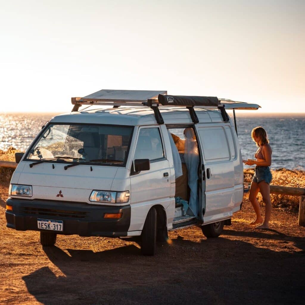 @theearthnsky_studios Woman camping in her white camper van at the beach