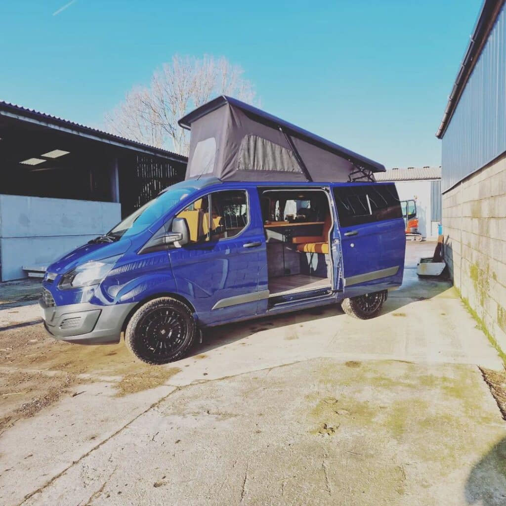 @tw_campers Blue camper van with pop top parked in a parking space