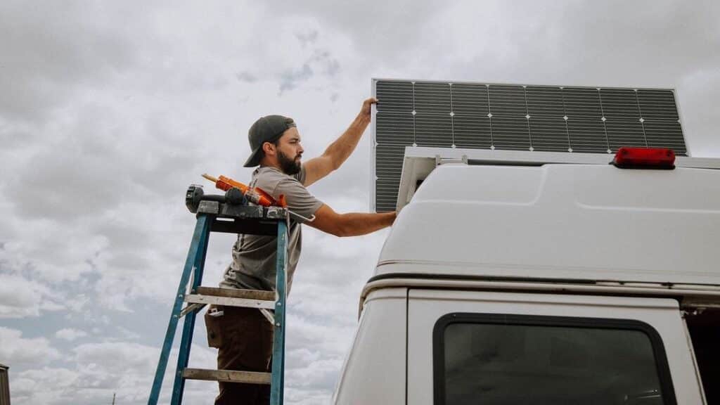 person on a ladder placing the best solar panels for van conversion. on the roof of his high top campervan