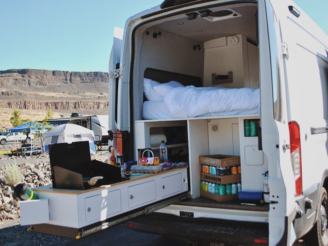 @cabanavans open back door of a van camper with platform bed and slide out kitchen kit extended