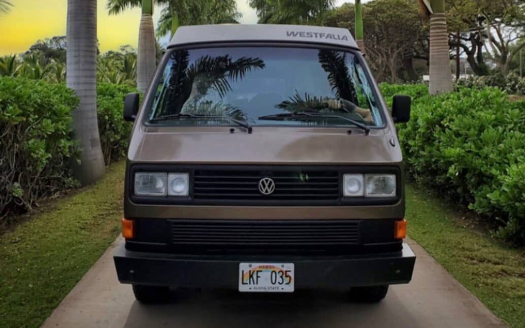 @mauiwesty vw camper van rental in a parking space surrounded by tropical plants