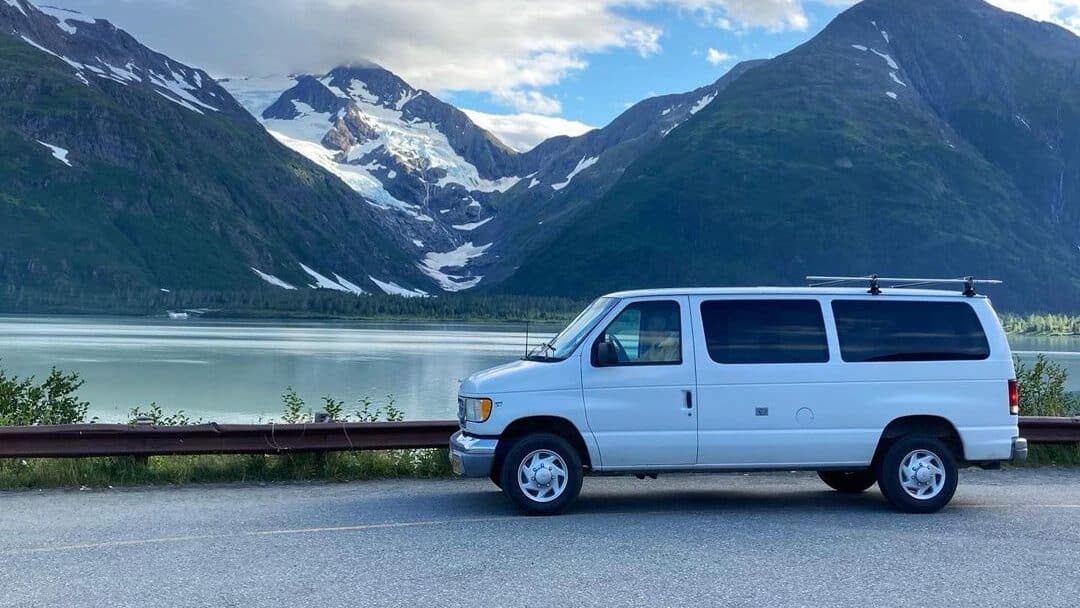 @northwestvancampers ford econoline camper rental parked on the side of a road near a lake
