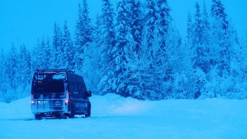 @riverwildcampervans alpine winter scene featuring a campervan covered in snow 
